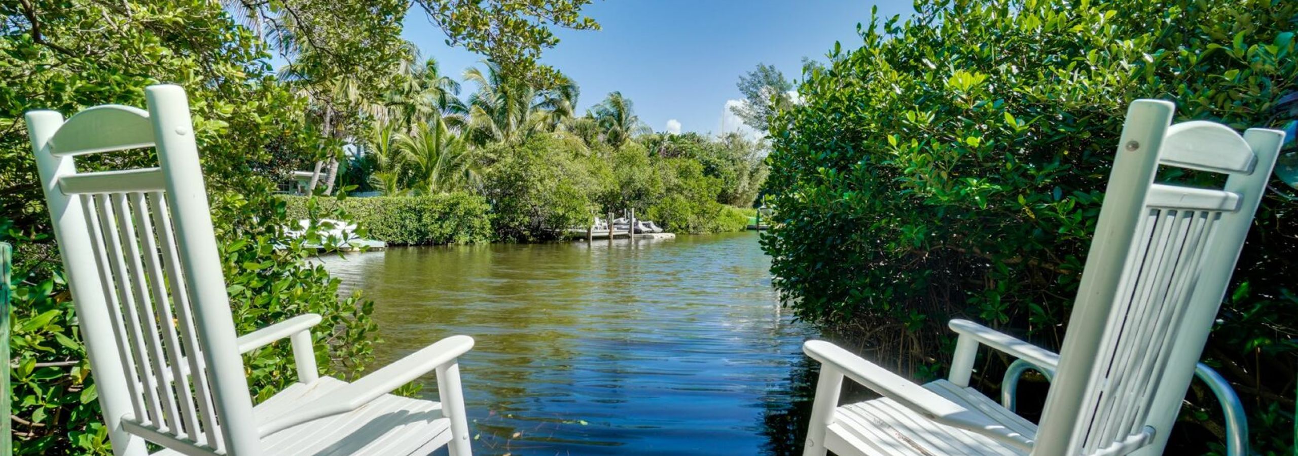 White Adirondack chairs on wooden dock overlooking peaceful waterway