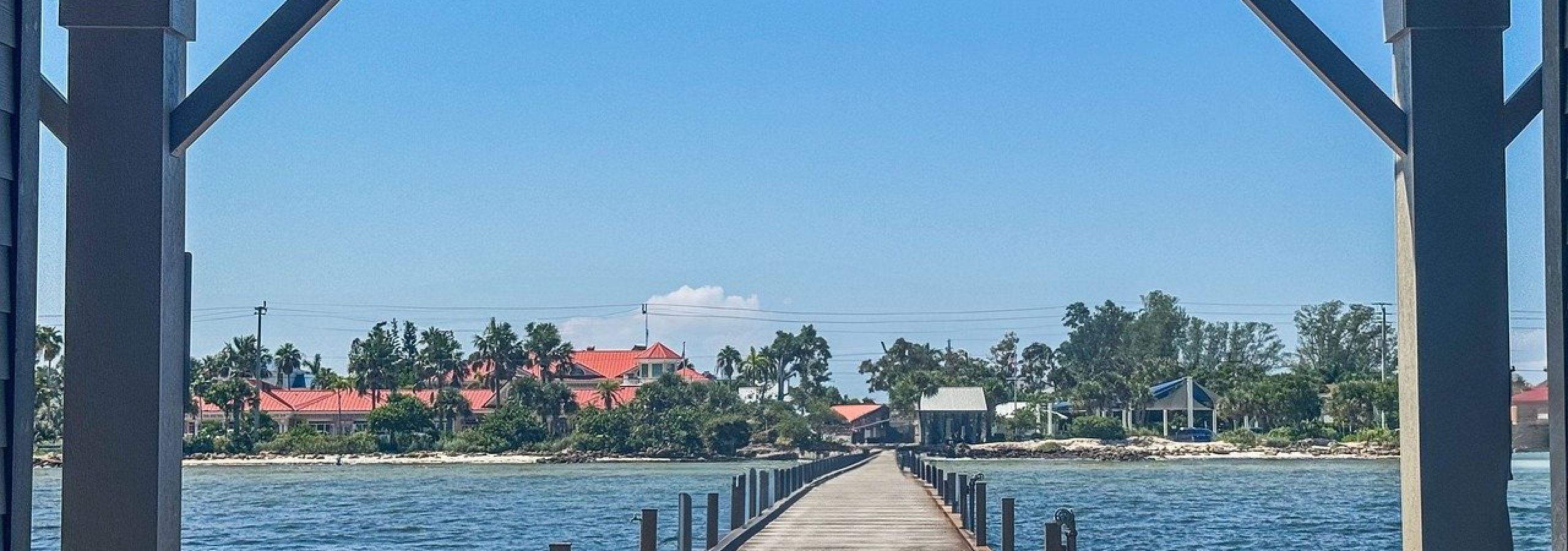 Wooden pier extending into turquoise water viewed through pavilion