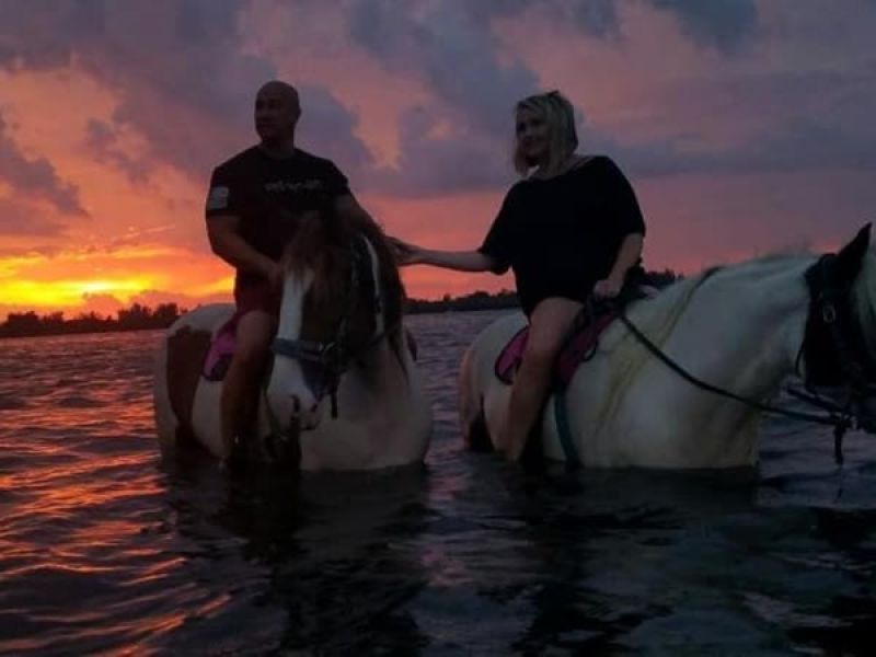 Couple horseback riding at ocean sunset