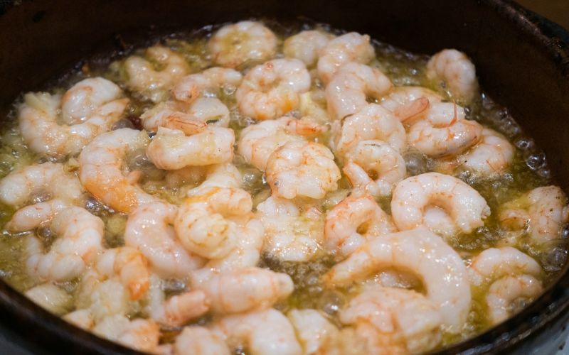 Pink shrimp sautéing in butter and garlic in dark skillet