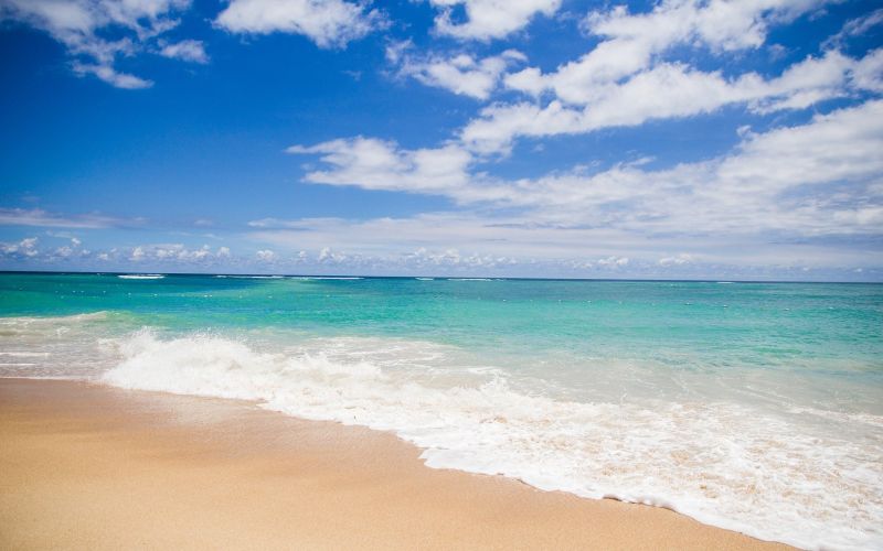 Turquoise water lapping sandy beach under blue sky