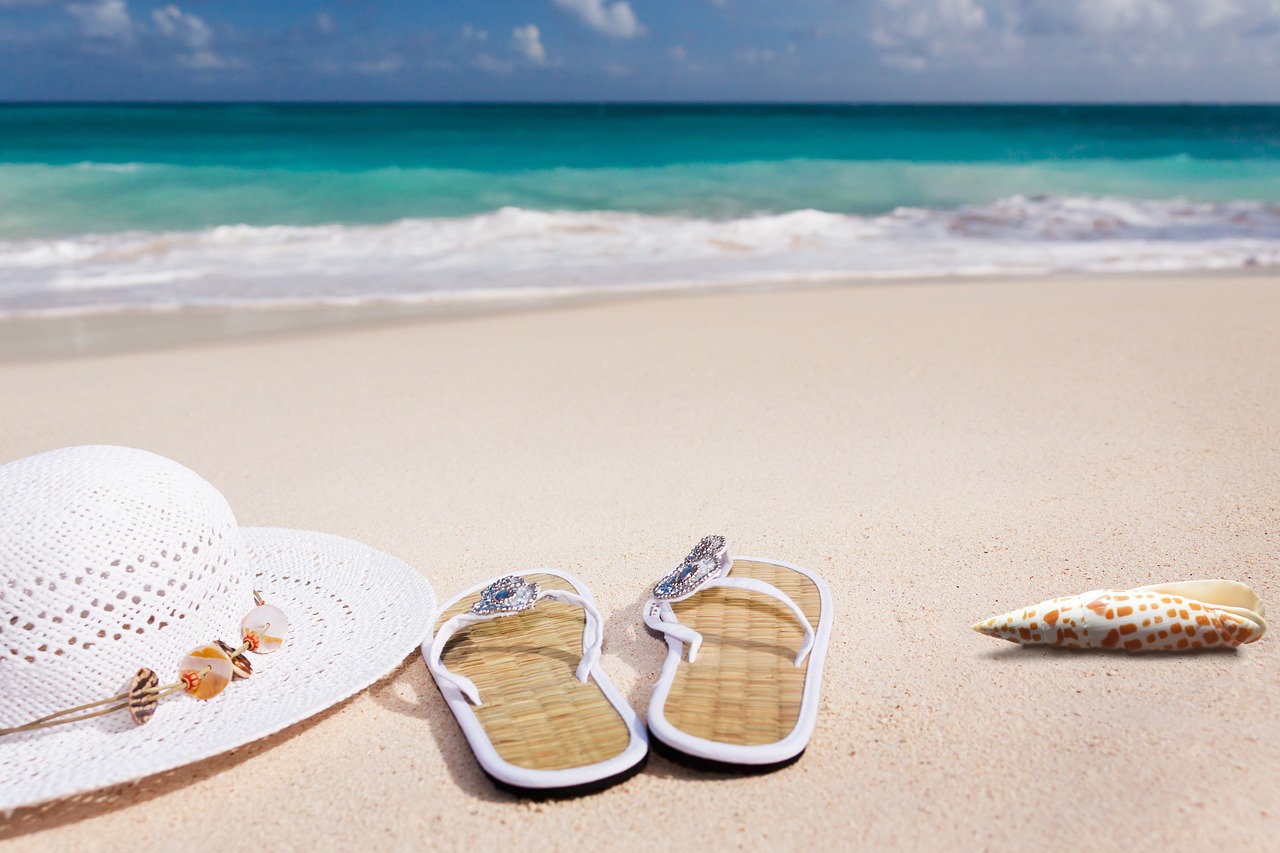 White sun hat, sandals and driftwood arranged on sandy beach