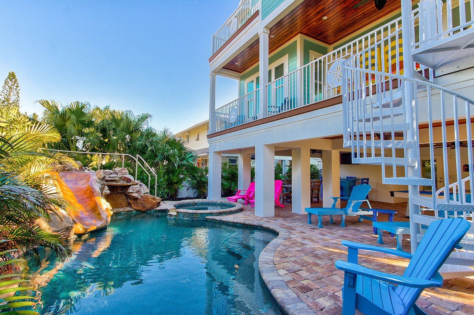 Vacation rental with blue pool, bright Adirondack chairs, tropicals