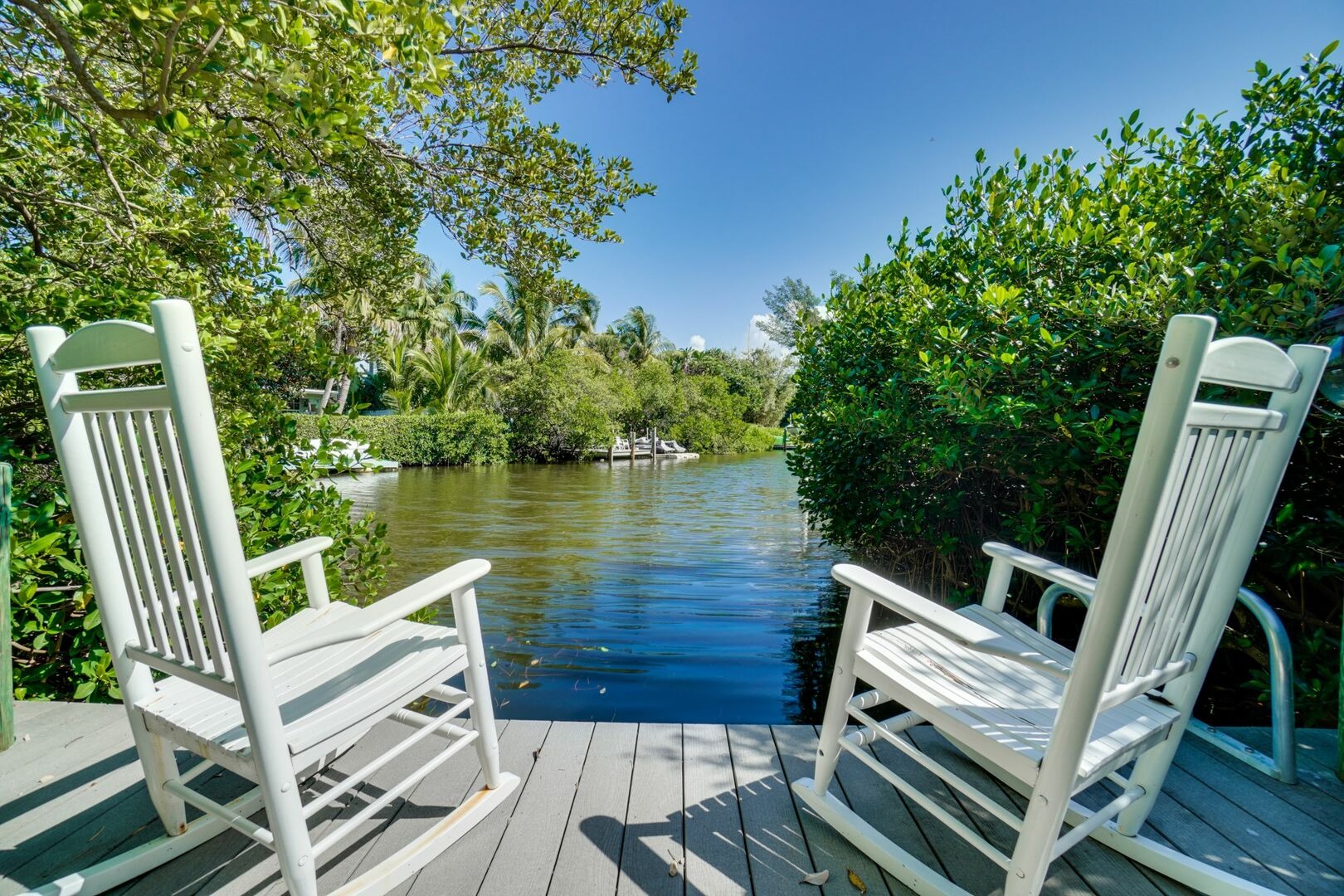 White Adirondack chairs facing waterway through trees