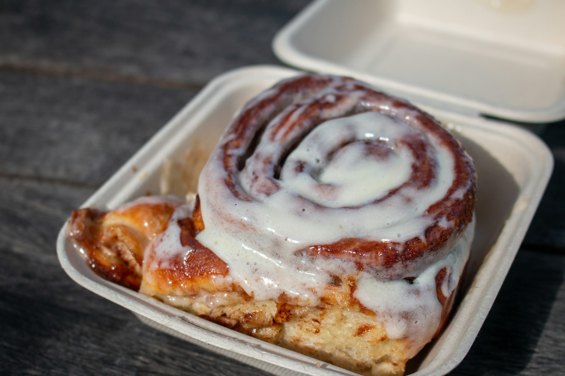 Frosted cinnamon roll pastry in white takeout container