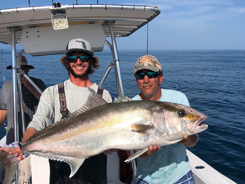 Two fishermen holding large caught snapper on boat