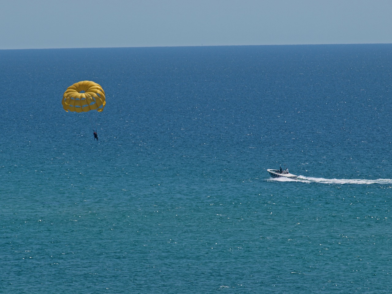 Parasailing over turquoise Gulf water near sailboat